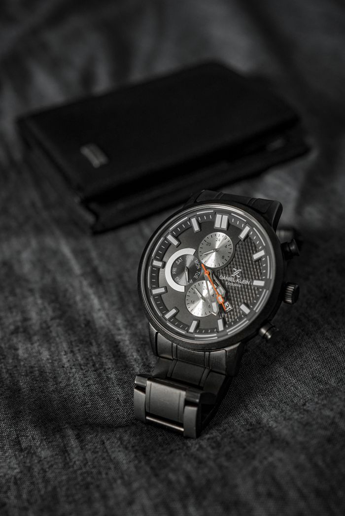 Close-up of a black wristwatch with metallic dial on a textured fabric background.